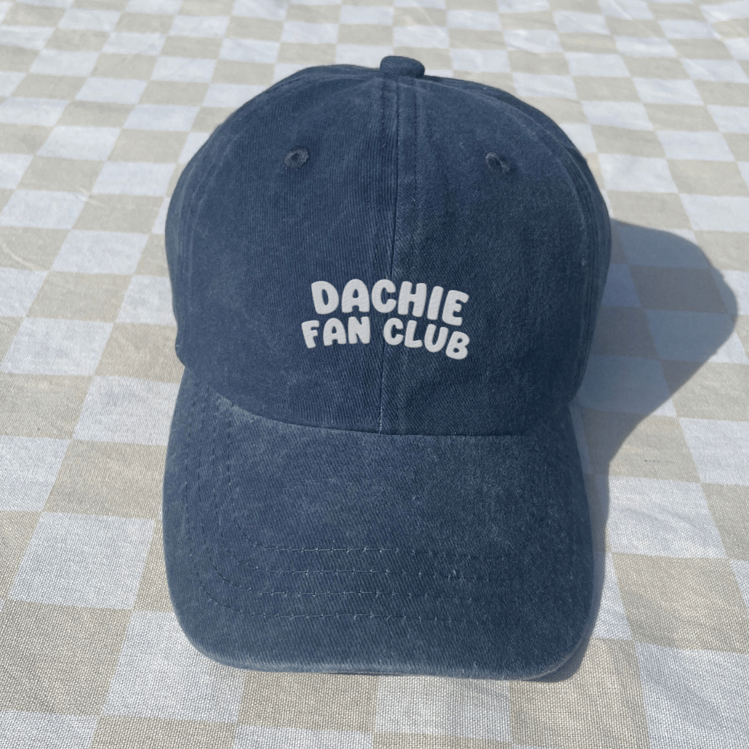 Navy blue cap with 'Dachie Fan Club' text on a checkered floor