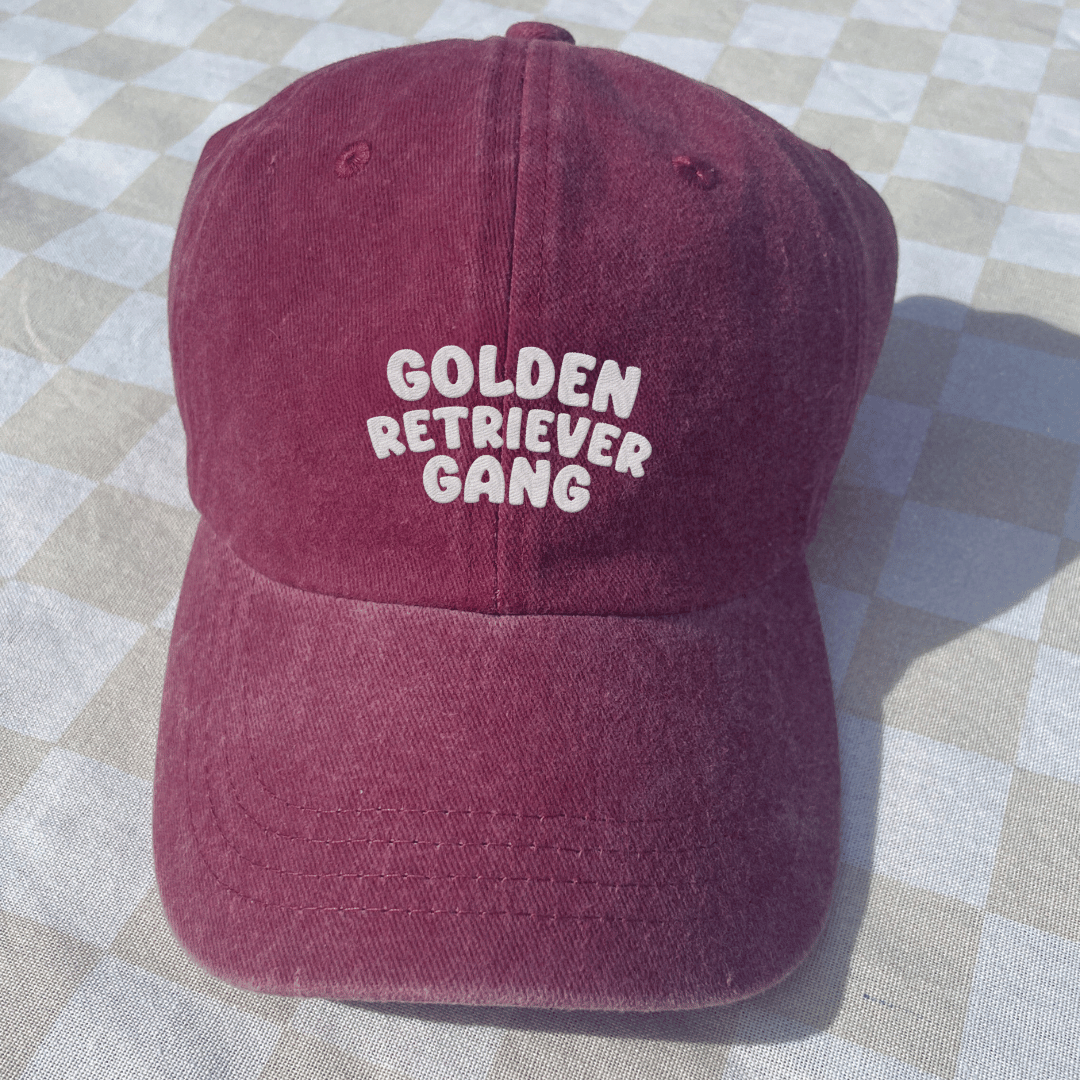 Maroon cap with 'Golden Retriever Gang' text on a checkered fabric background