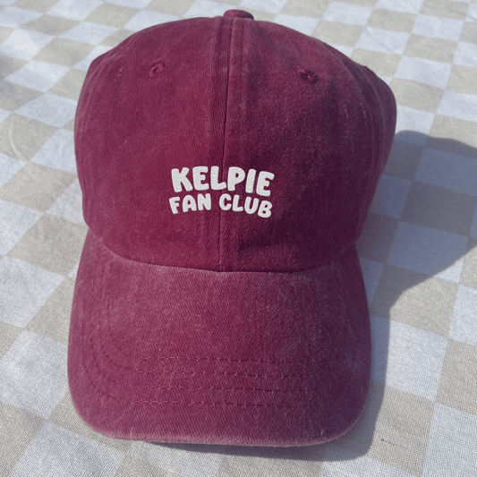 Maroon cap with 'Kelpie Fan Club' text on a checkered fabric background