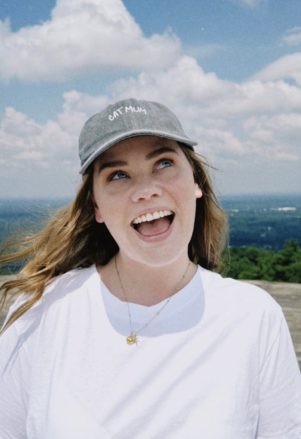 Girl in white t shirt wearing grey cat mum cap looking happy 