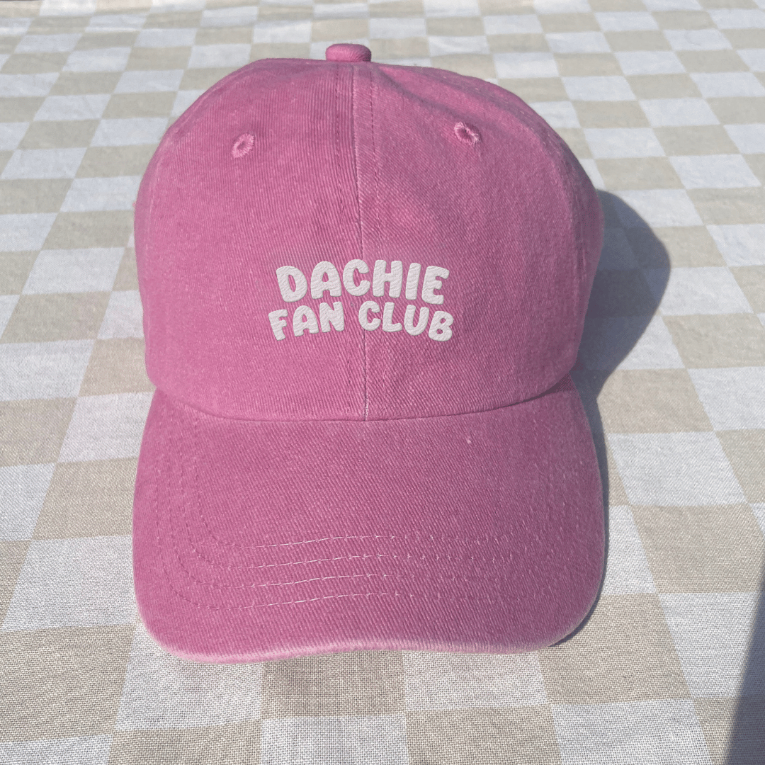 Pink cap with 'Dachie Fan Club' text on a checkered floor