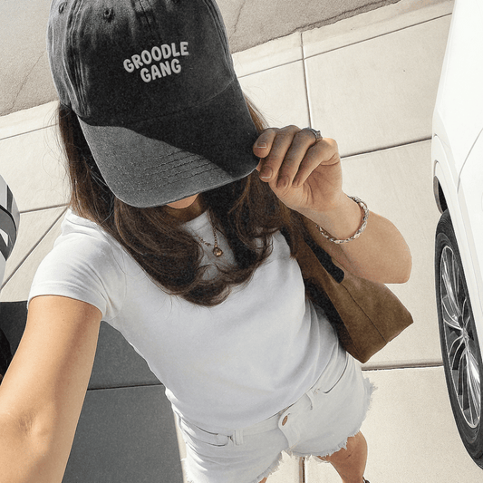 Person wearing a black cap with 'GROODLE GANG' text, standing next to a car.