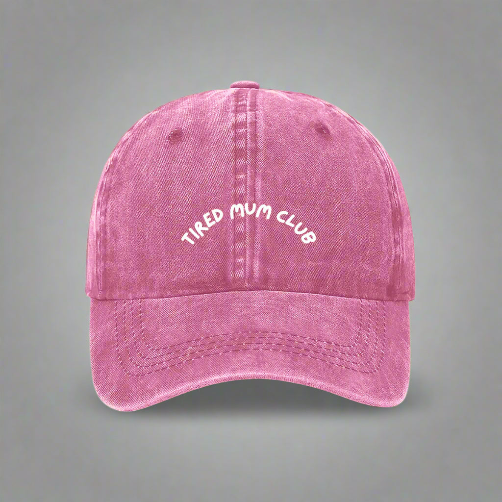 A pink baseball cap with 'TIRED MUM CLUB' embroidered in white on the front.