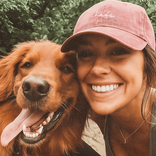 Woman and dog smiling together with a pink cap that says chaos