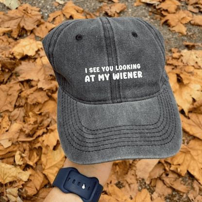 A gray baseball cap with the text 'I SEE YOU LOOKING AT MY WIENER' embroidered in white.
