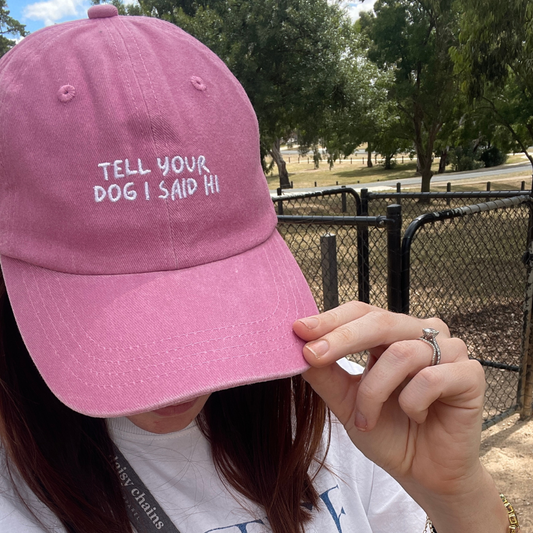 Woman wearing a pink cap embroidered 'tell your dog i said hi.' She is at the dog park and happy. Great gift idea for dog lovers in australia