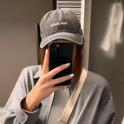A person wearing a gray baseball cap with 'Wiener Mum' text on it.