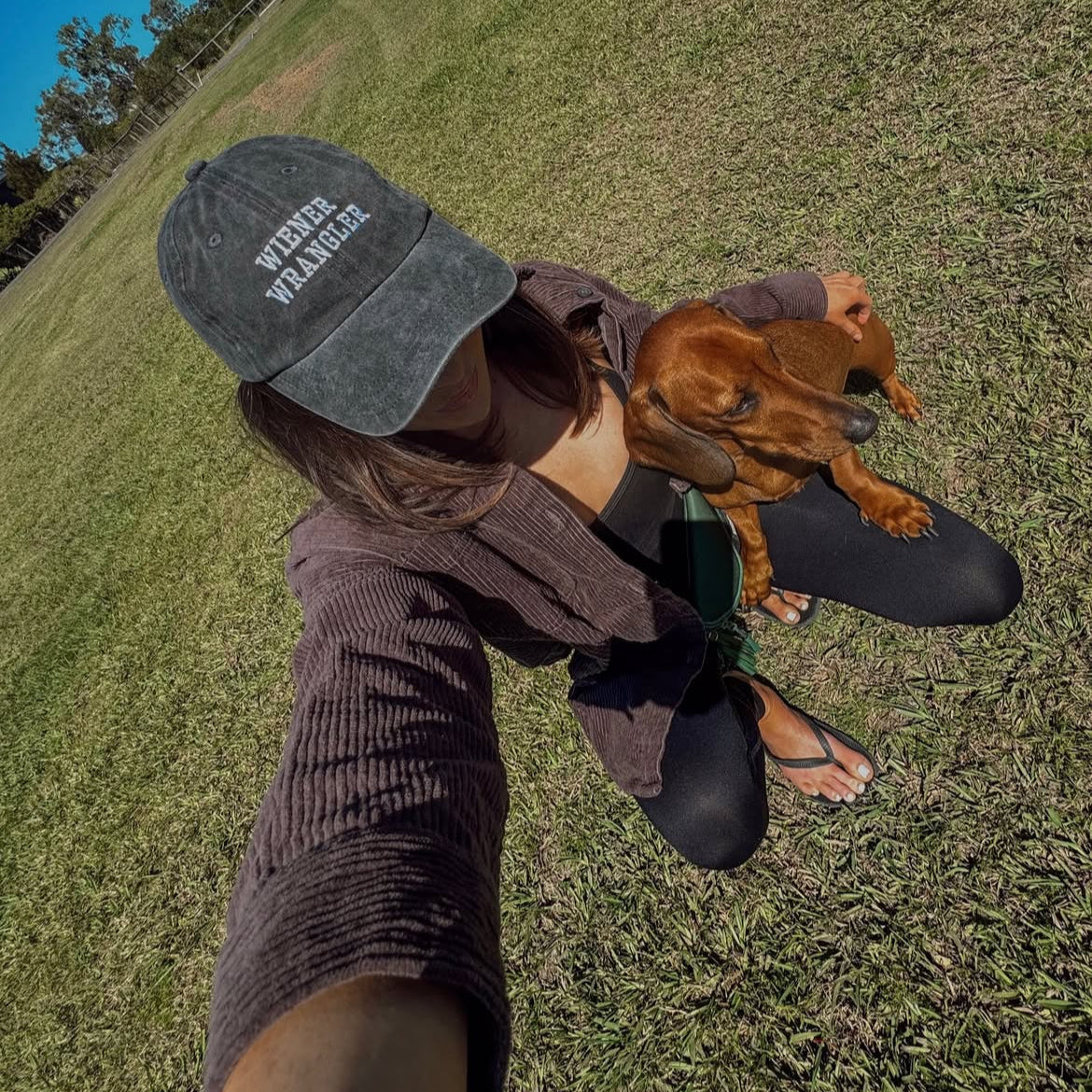girl and her dachshund. she is wearing a cap that says wiener wrangler